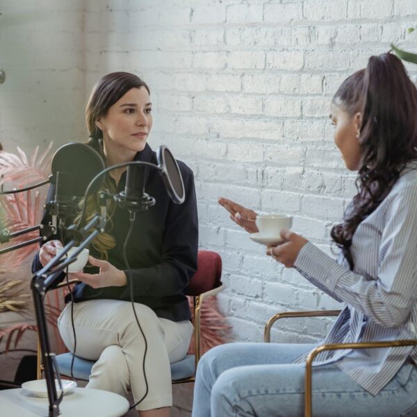 women sit in chairs in front of podcast mics