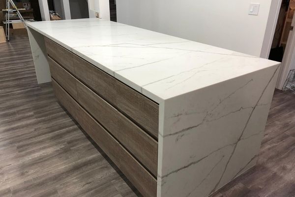 Close-up of a contemporary kitchen island with a white marble waterfall countertop and light wood custom cabinetry.