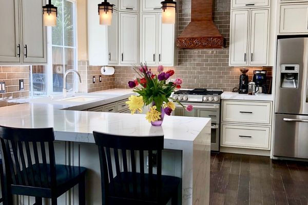 Modern kitchen remodel featuring white waterfall countertops, white shaker cabinets, a subway tile backsplash, and a luxury copper range hood.