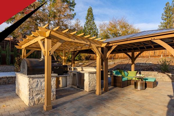 A beautifully crafted wooden pergola over a stone outdoor kitchen area, showcasing custom deck and outdoor living construction by ATA Construction.